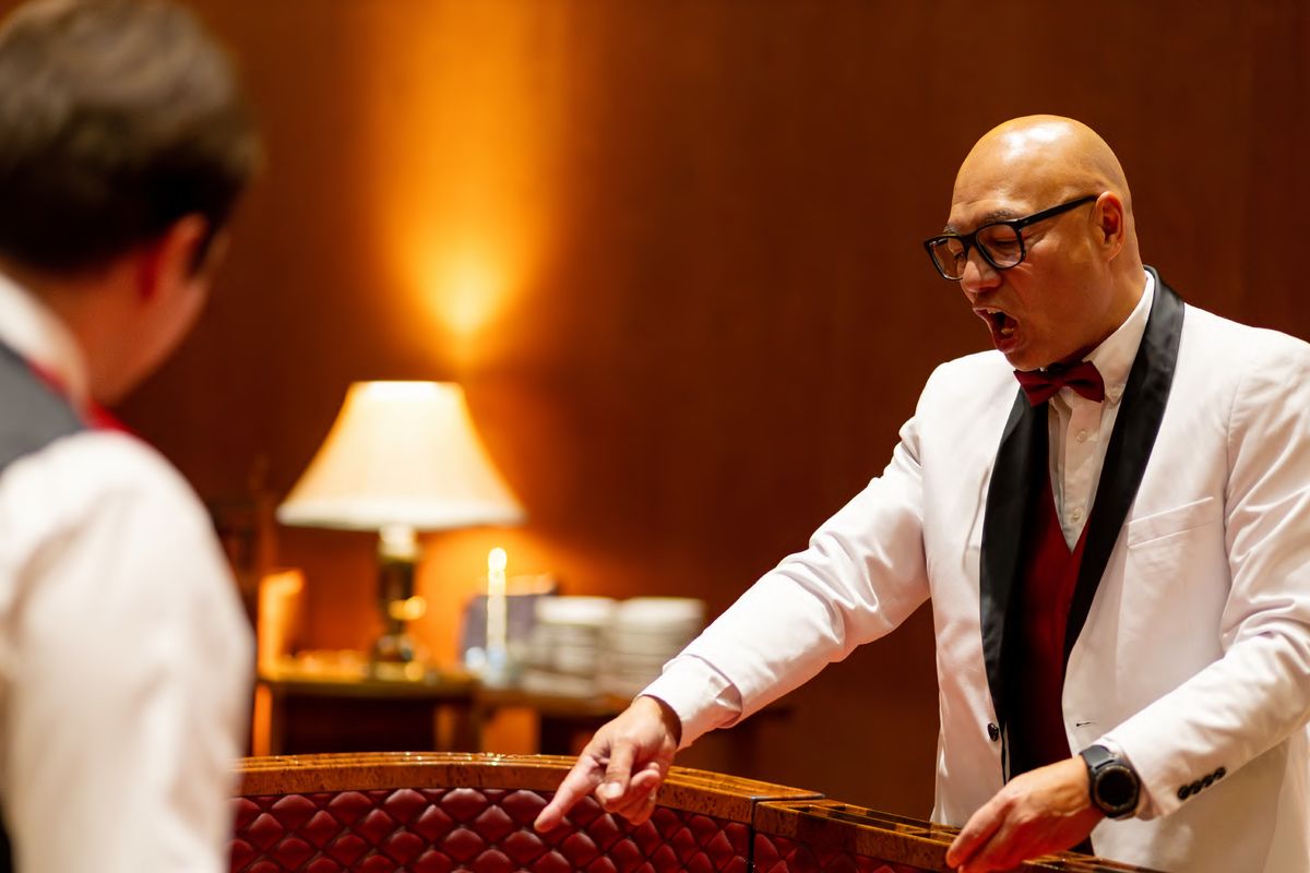 A host in a white dinner jacket running a casino table at a company holiday party, photographed by Dario Hudon