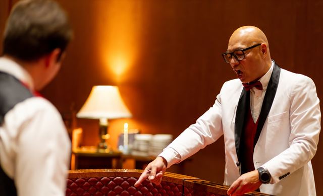 A host in a white dinner jacket running a casino table at a company holiday party, photographed by Dario Hudon