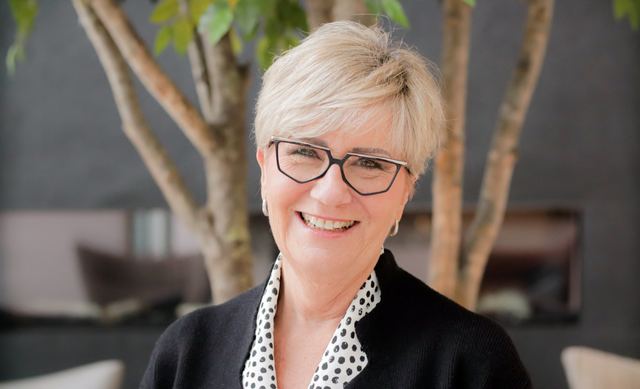 A headshot of a smiling woman with short blonde hair and glasses, photographed by Dario Hudon