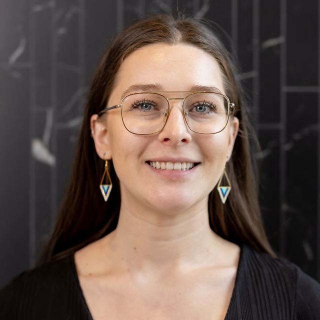 A headshot of a smiling woman with glasses on a dark background, photographed by Dario Hudon