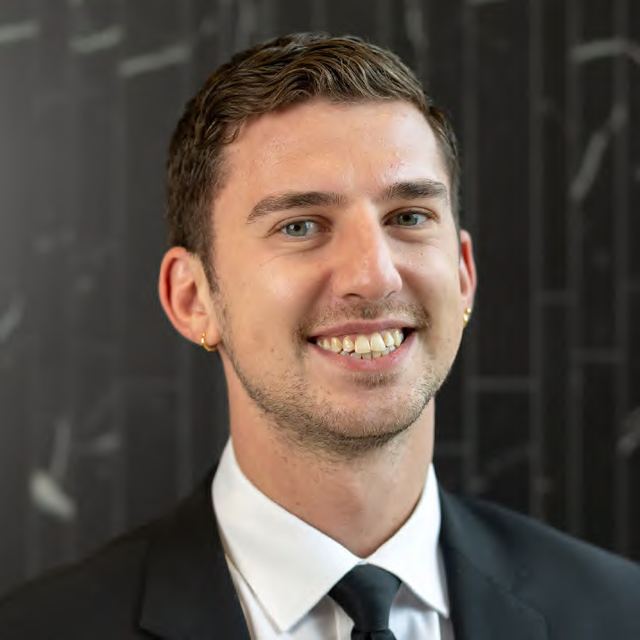 A headshot of a smiling man in a suit and tie, photographed by Dario Hudon