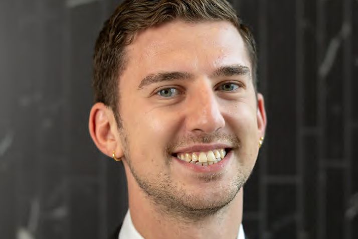 A headshot of a smiling man in a suit and tie, photographed by Dario Hudon