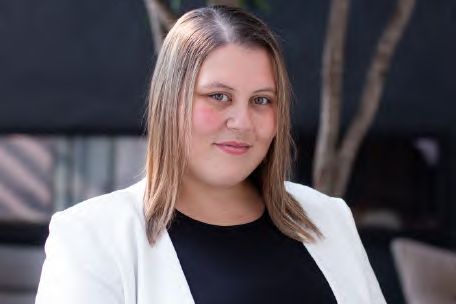 A headshot of a smiling woman in a white blazer, photographed by Dario Hudon