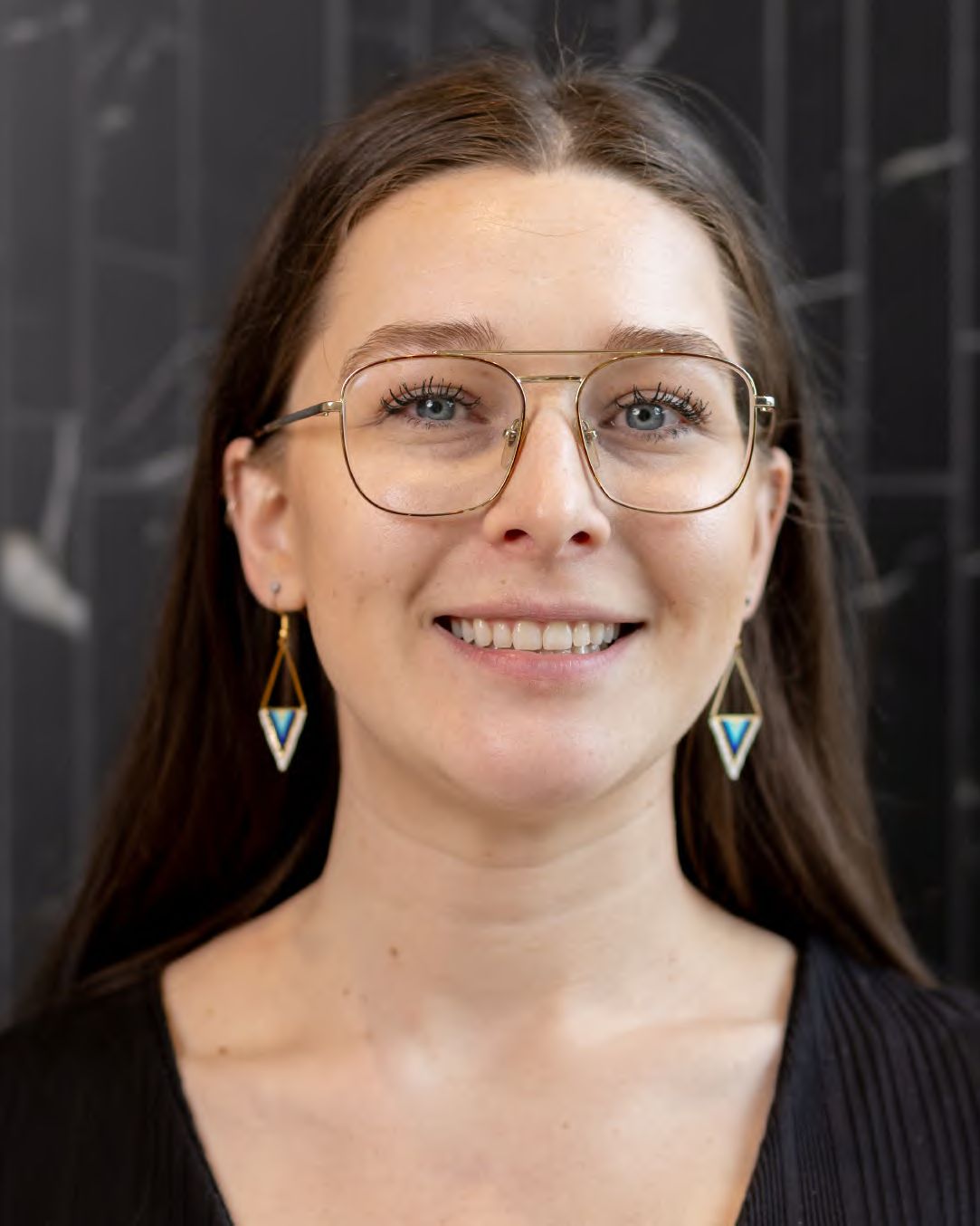 A headshot of a smiling woman with glasses on a dark background, photographed by Dario Hudon